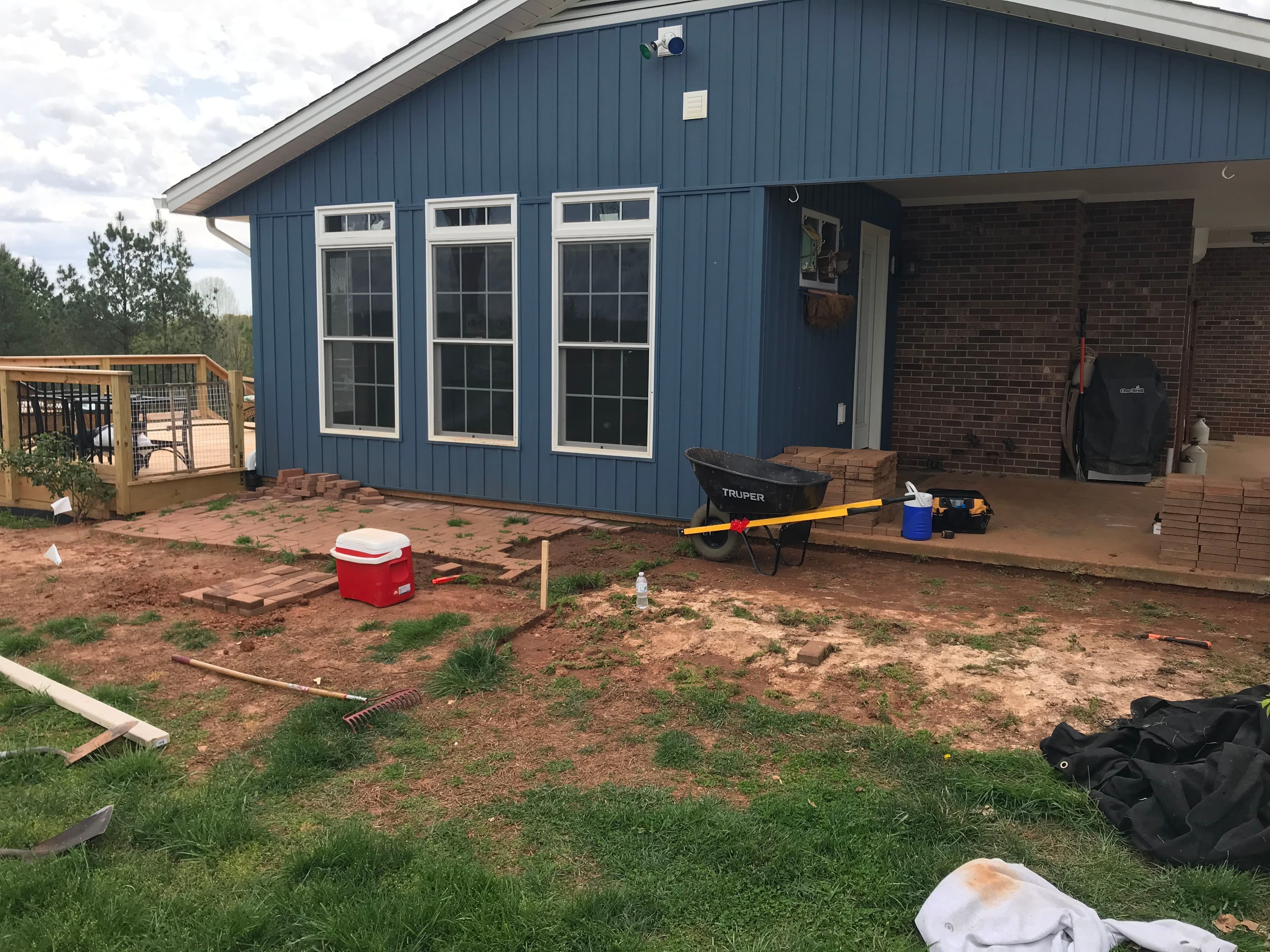 Home renovation site with a blue house, wheelbarrow, and landscaping materials.