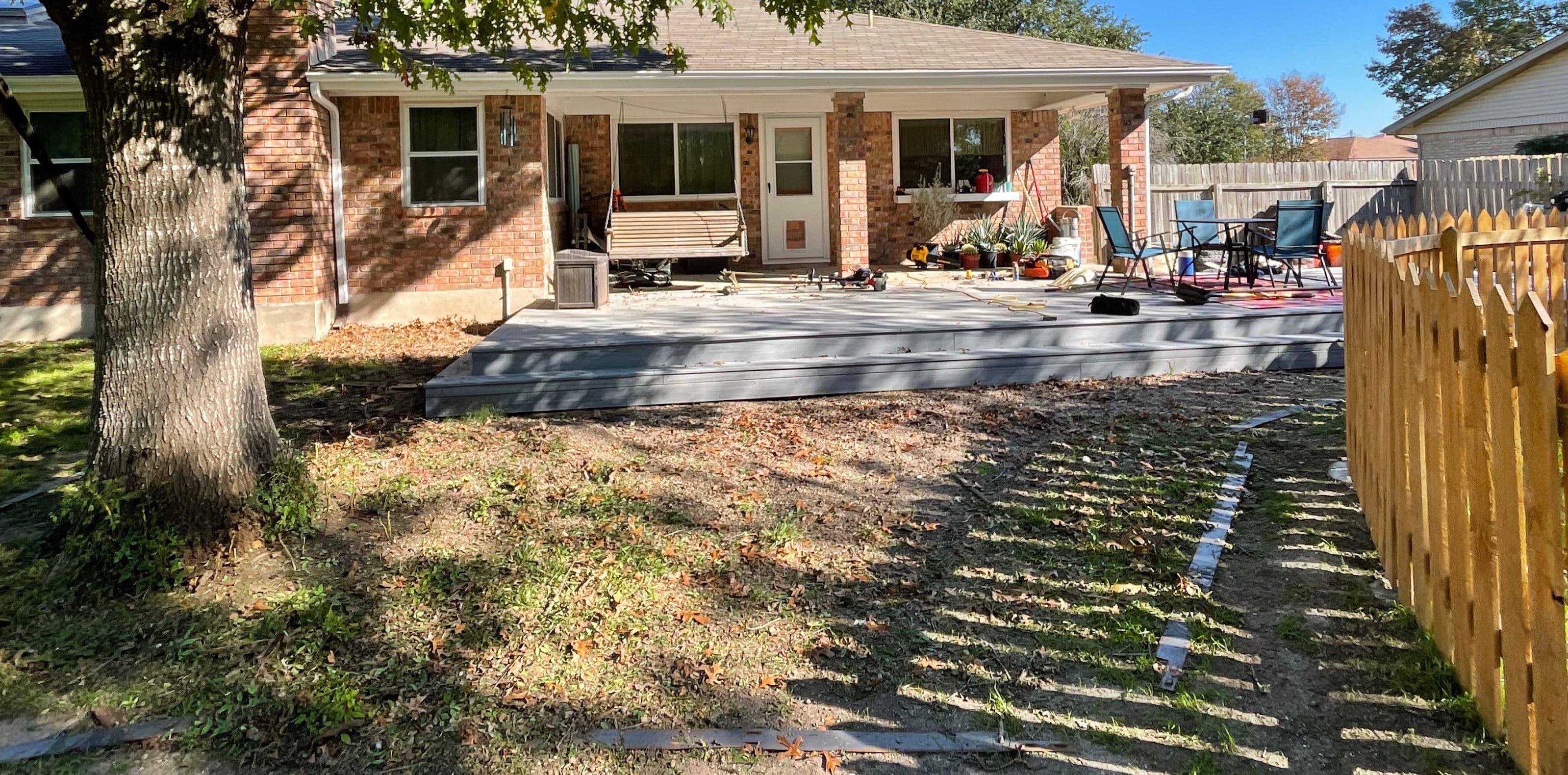 Backyard with wooden deck, swing, garden furniture, and freshly landscaped area. Sunny day.