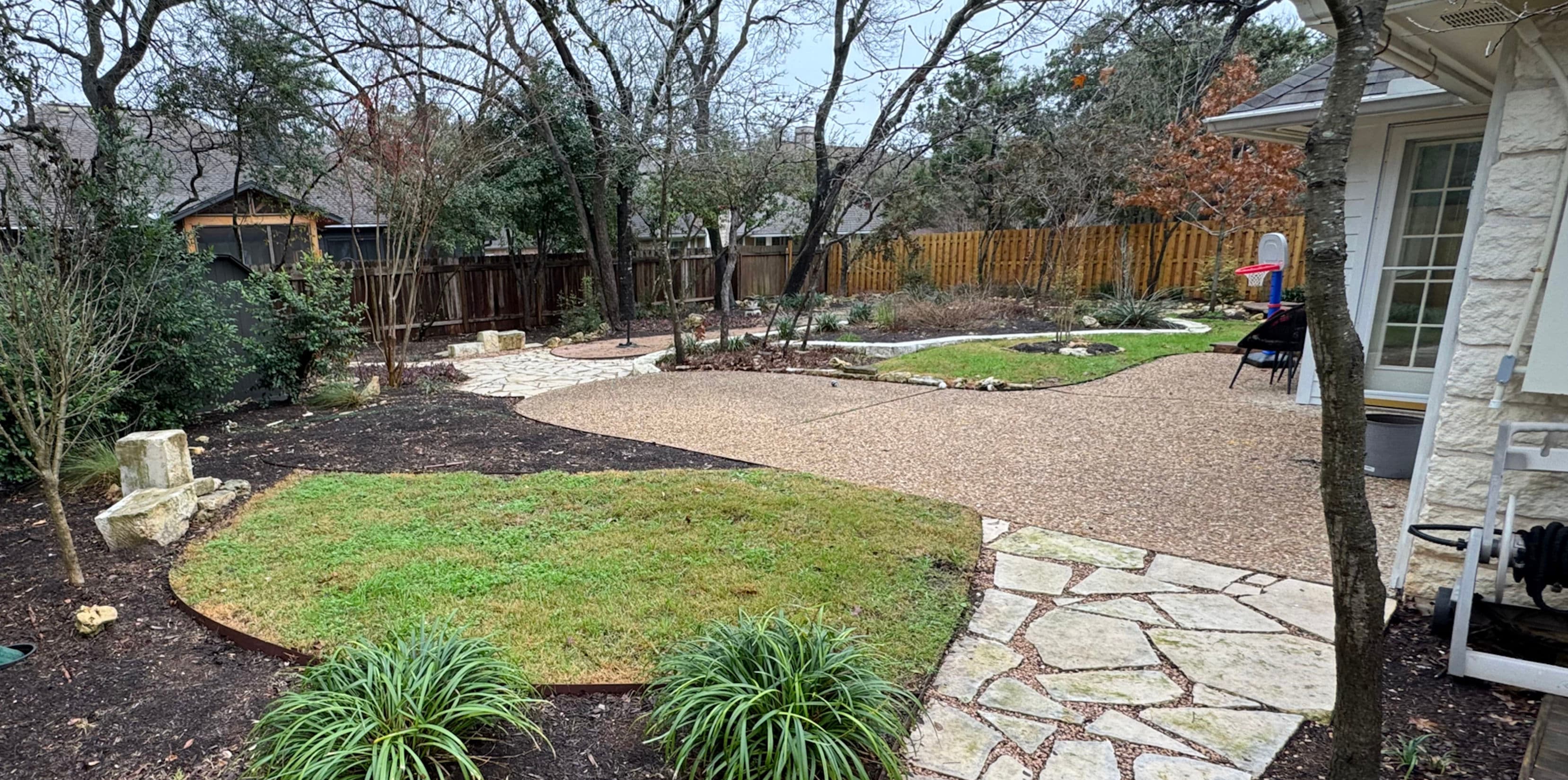 Lush backyard garden design featuring stone paths, grass, and diverse landscaping elements.