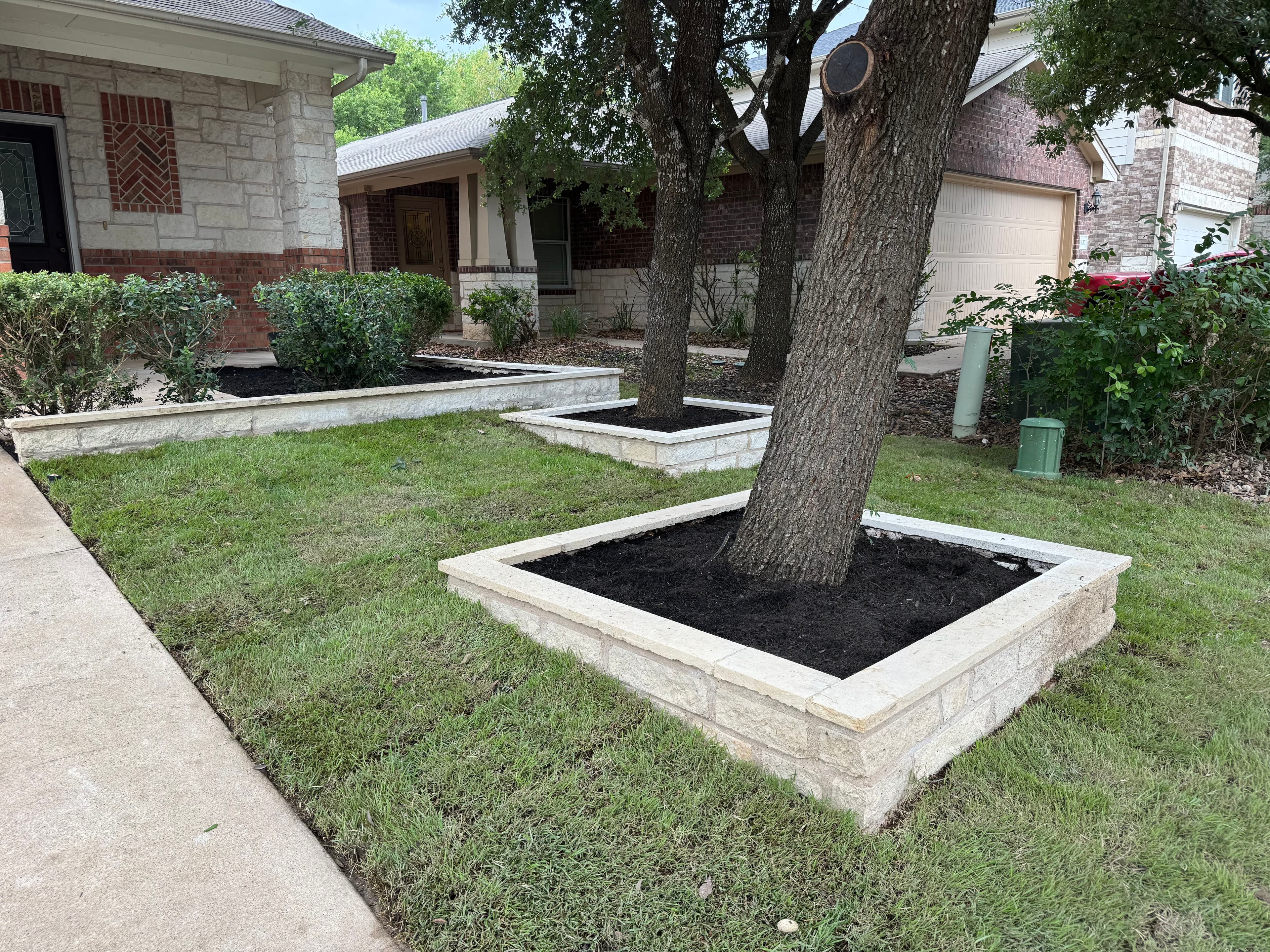 Landscaped yard with stone-bordered tree beds and freshly mulched soil, enhancing curb appeal.