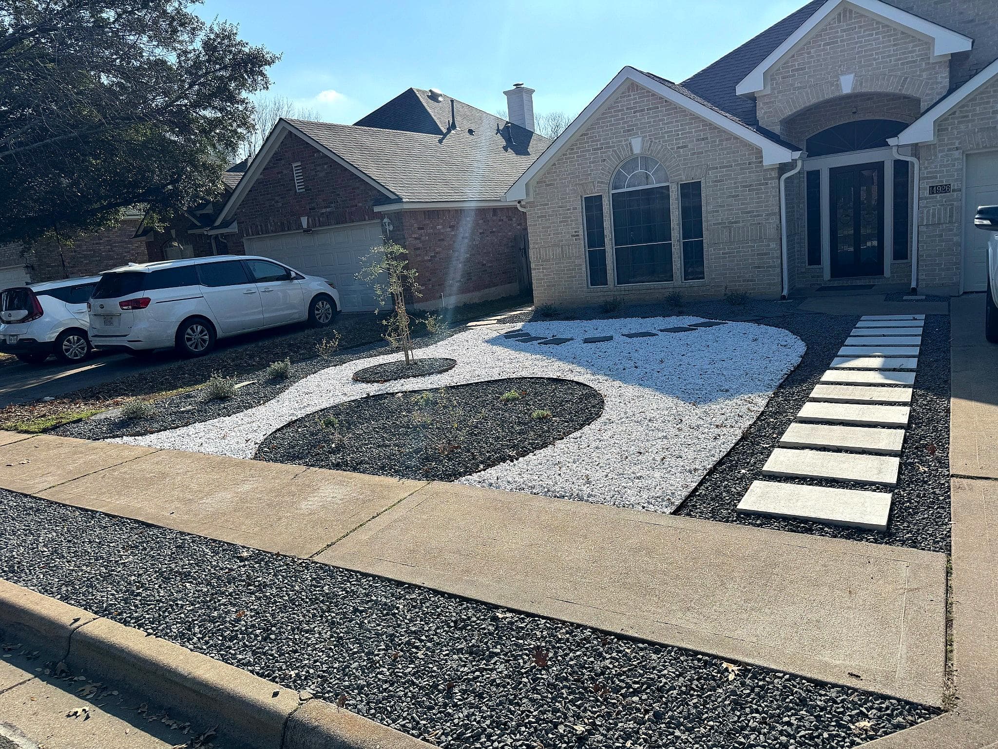 Modern front yard landscaping with white gravel, stepping stones, and minimalist design elements.