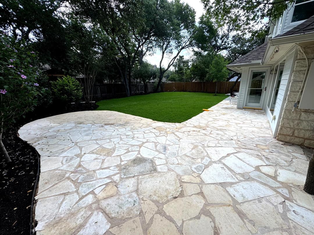 Stone patio leading to manicured lawn surrounded by trees in a backyard setting.