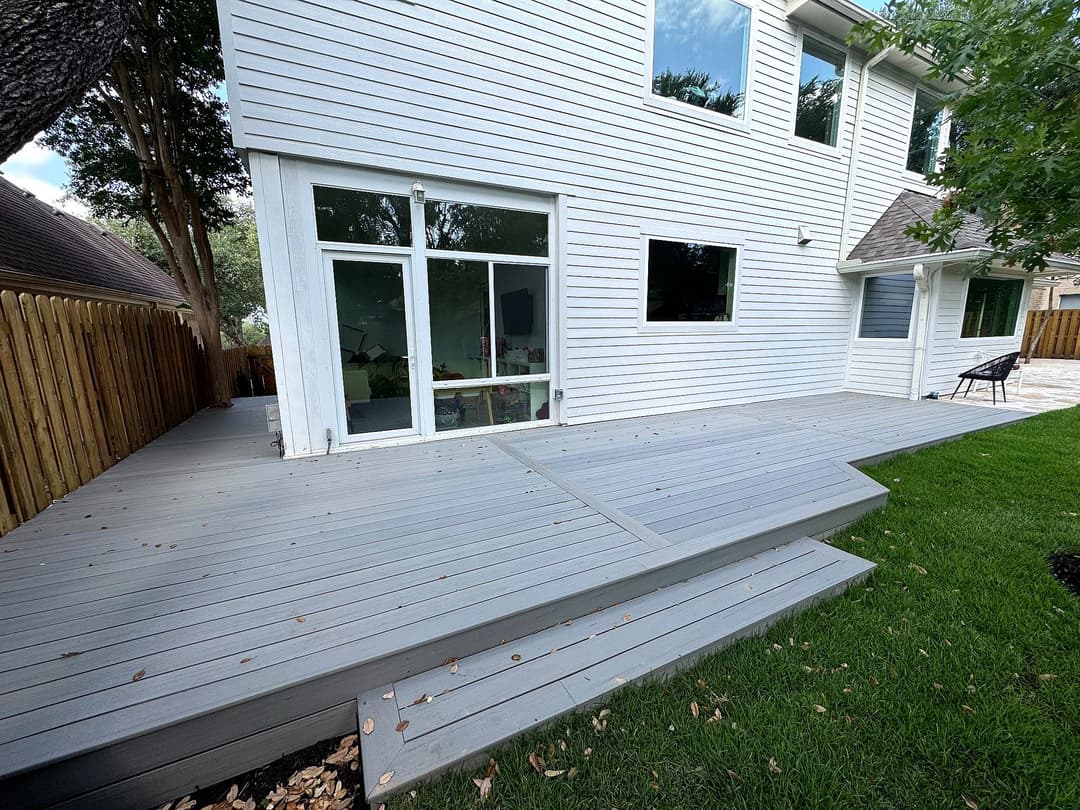 Modern gray composite deck with steps leading to a contemporary home and green lawn.