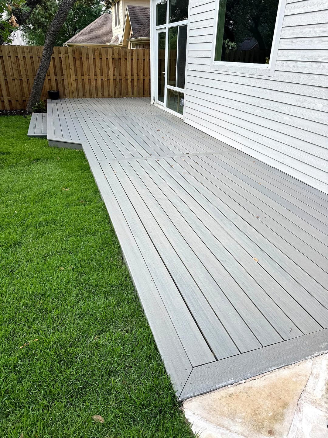 Modern gray composite deck beside a well-maintained lawn and wooden fence.