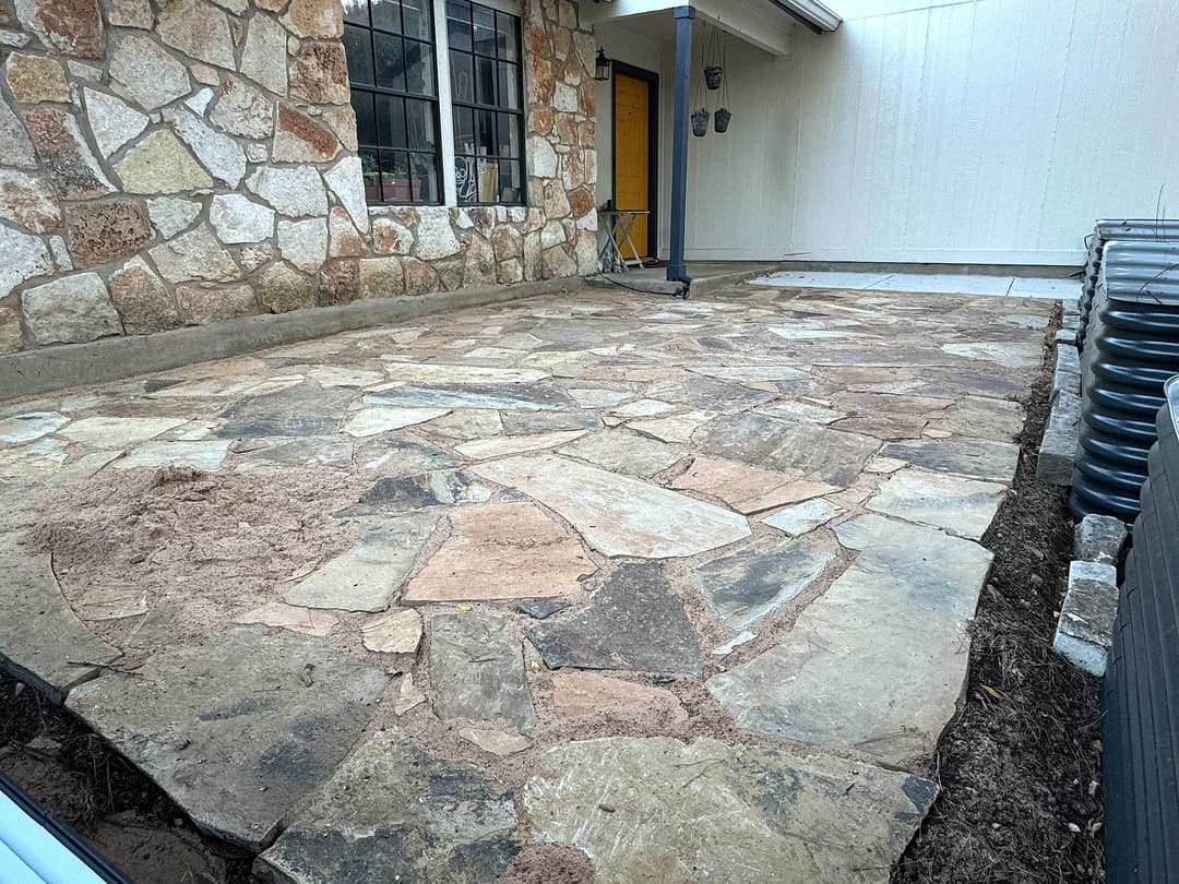 Natural stone patio installation with irregularly shaped stones and adjacent building.
