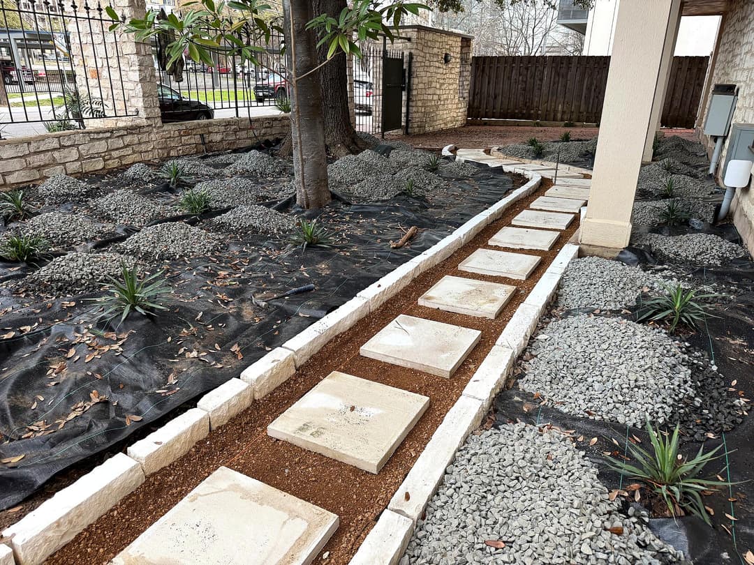 Garden pathway with stepping stones, gravel beds, and landscaping fabric surrounded by plants.