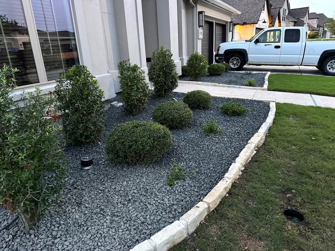 Front yard landscaping with rounded shrubs, decorative gravel, and a white pickup truck.