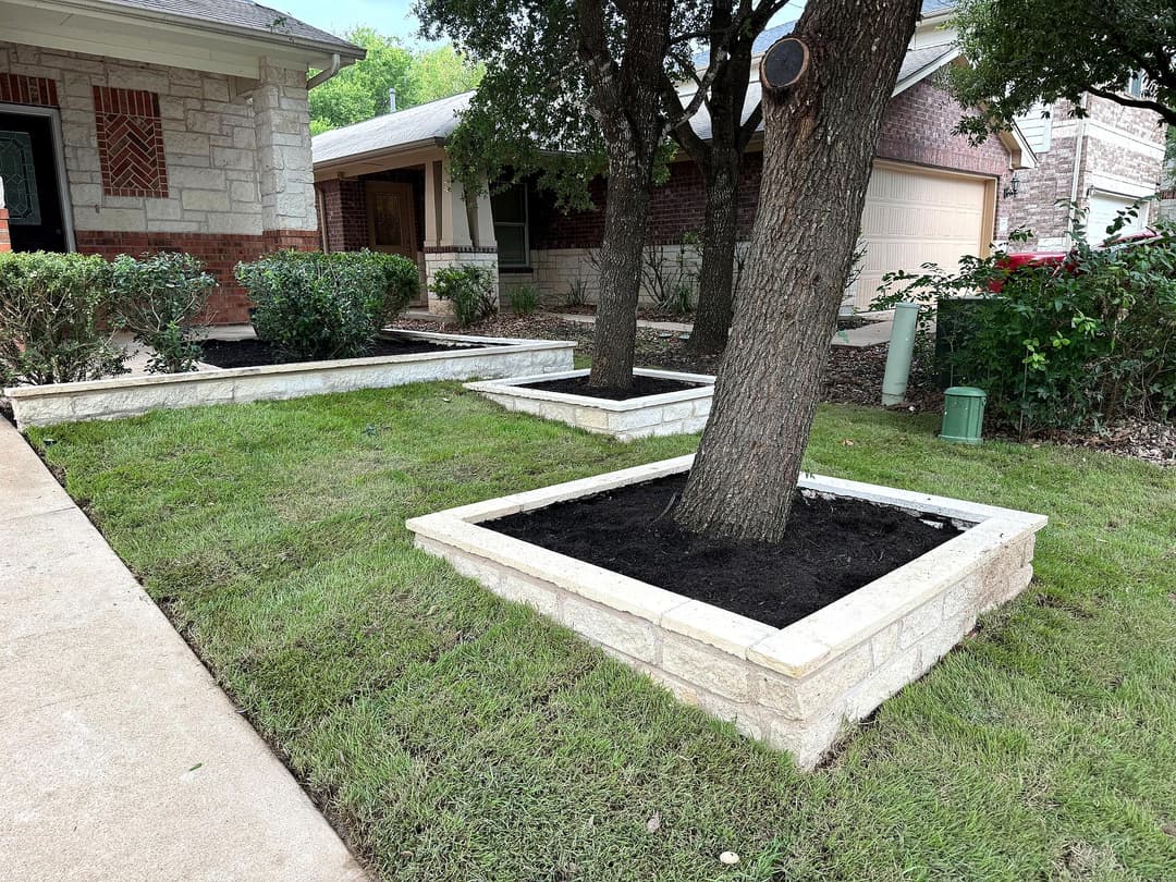 Landscaped front yard with stone-bordered planting beds around trees and fresh mulch.
