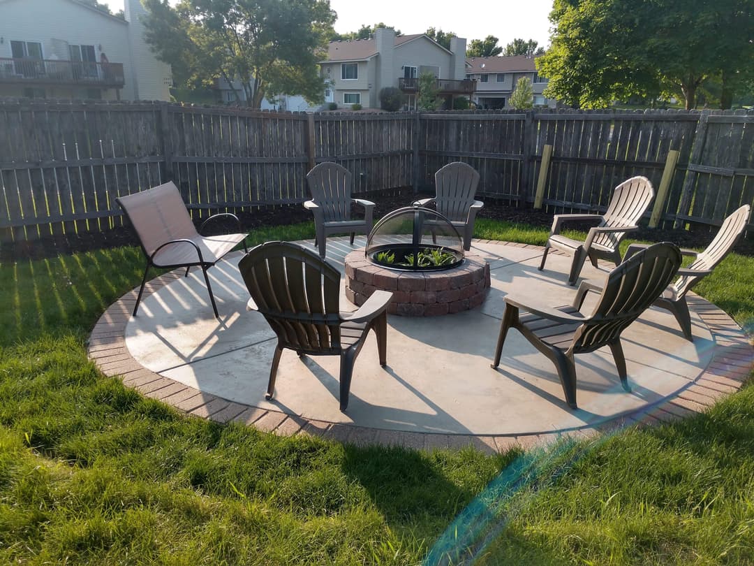 Backyard fire pit area with circular seating and green grass in a residential setting.