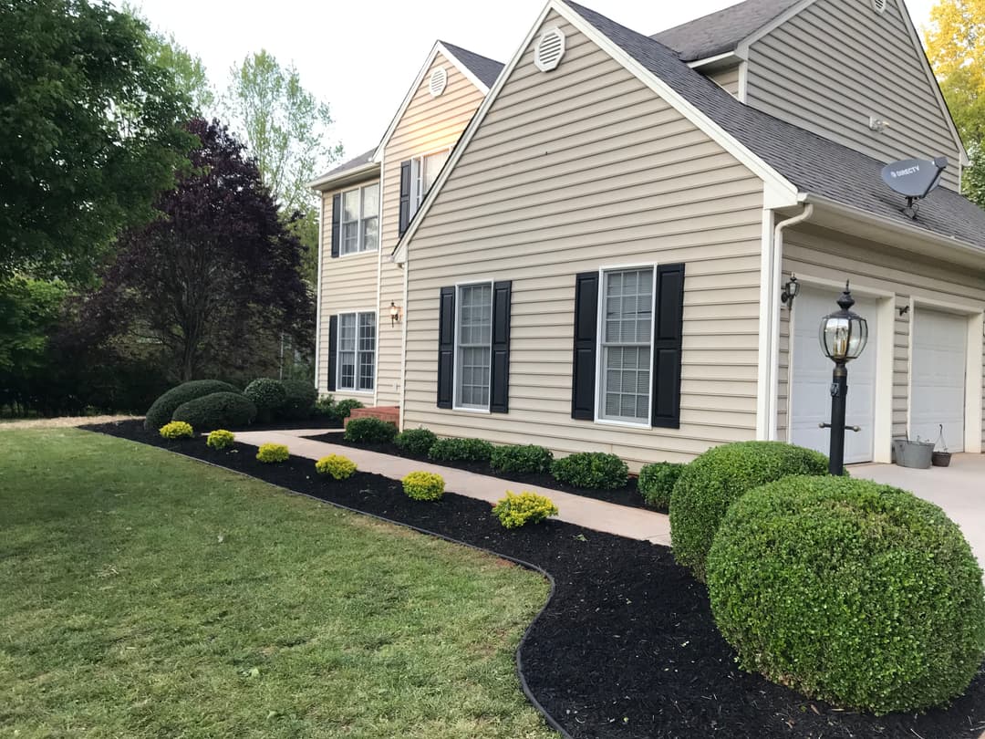 Well-maintained home exterior with landscaped garden, manicured bushes, and pathway.