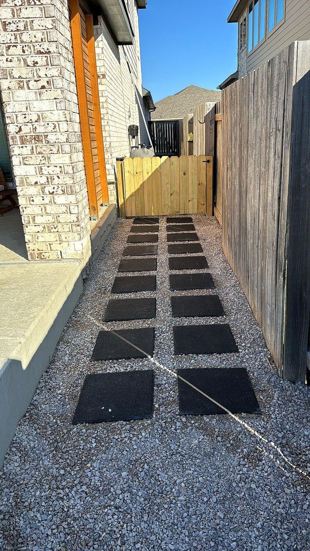 Stone pathway lined with black pavers in a residential backyard, leading to a wooden fence.